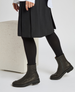 A pair of black, mid-calf leather boots with side zippers, a slightly rounded toe, and a sturdy rubber sole, worn with black tights and a black skirt. 2