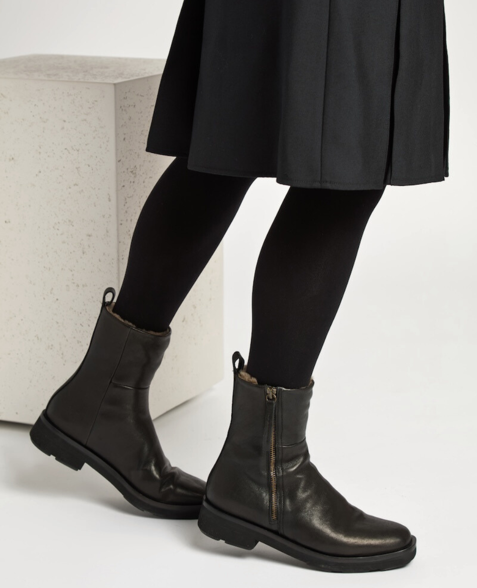 A pair of sleek, black leather ankle boots with side zippers, a slightly squared toe, and a low, sturdy heel, featuring a smooth, polished texture and a pull tab at the back.