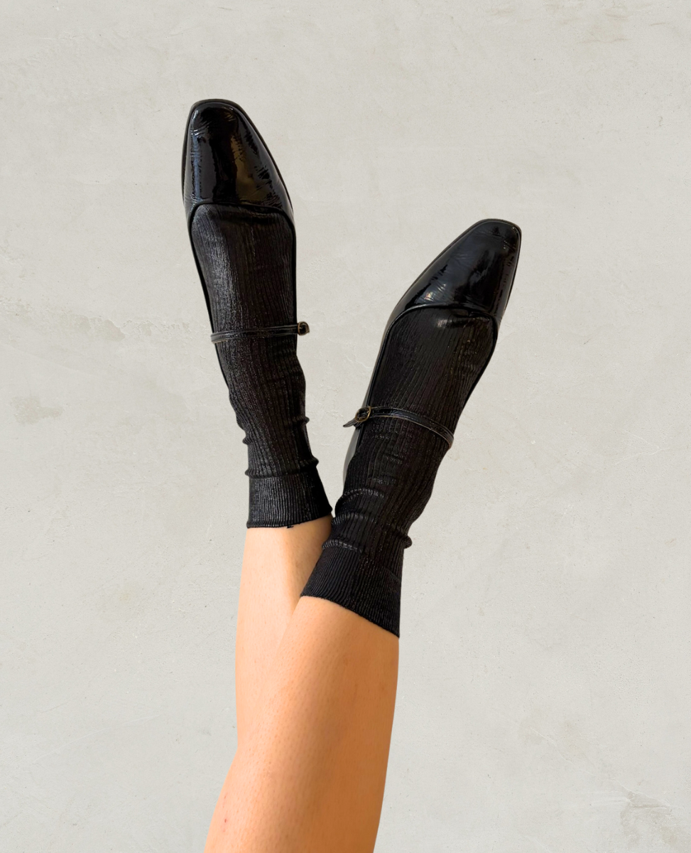 Black patent leather mary-janes and Maria La Rosa metallic black socks on a plain background