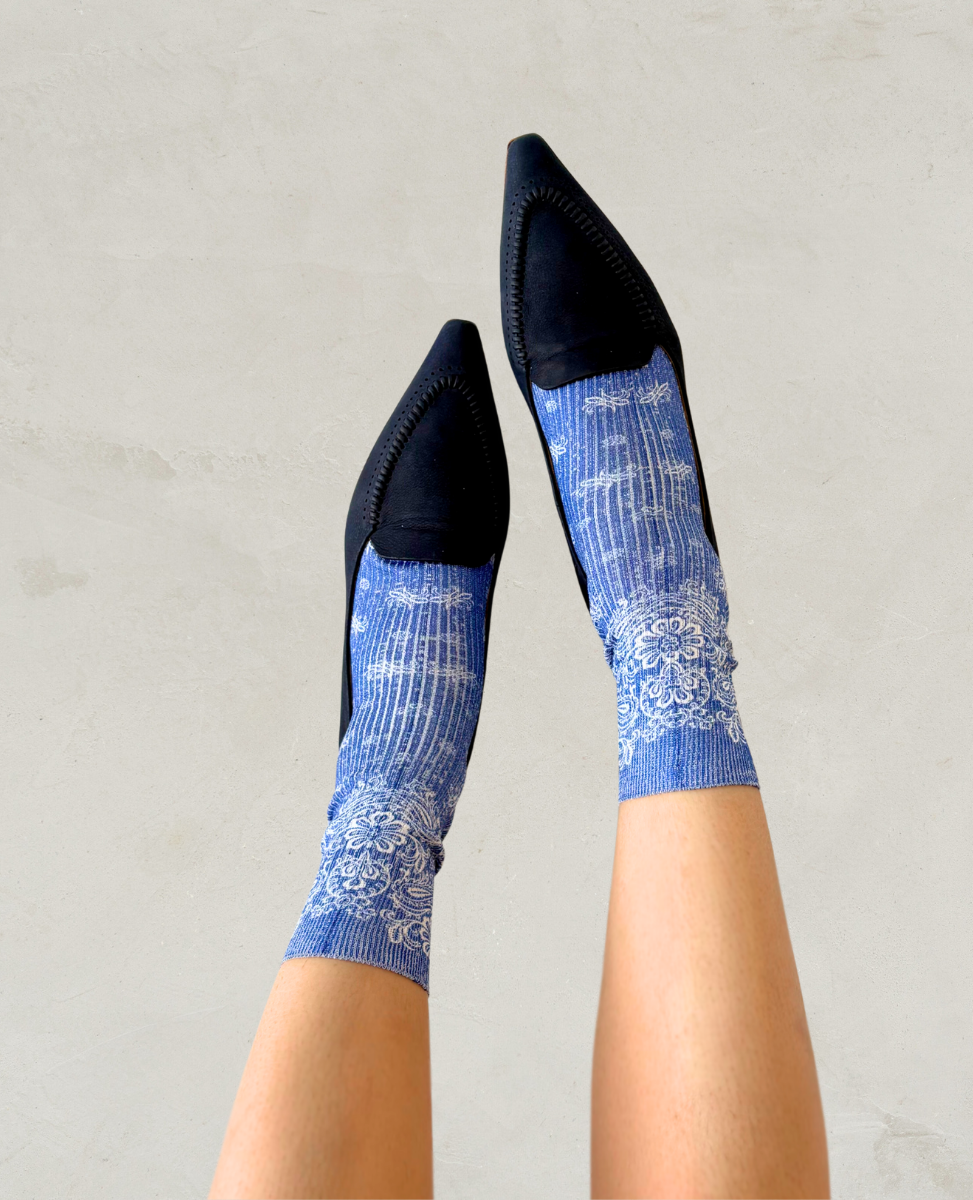 Pair of bue socks with white paisley bandana pattern shown on the foot with a pair of Coclico navy blue pointed loafers