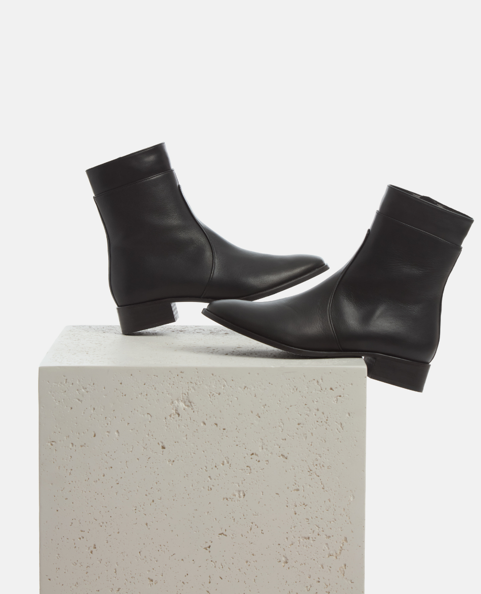 Black ankle boots on a light gray cube with a white background