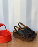 Coclico Moska Wedge in Deep Sea leather: Huarache inspired wedge sandals on a table with orange art.. 7