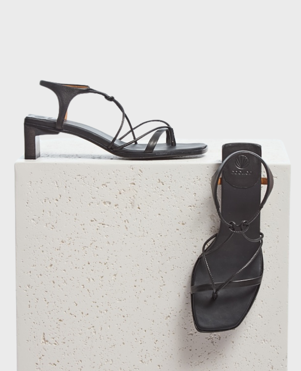 A pair of sleek black sandals with a square toe, thin straps, and a low block heel, featuring a minimalist design and smooth leather texture.