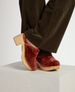 A pair of clogs with a chunky wooden heel and platform, featuring a rich autumnal pink shearling upper, worn with dark olive pants. 3