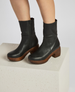 Black leather ankle boots with a smooth texture, featuring a side zipper, a rounded toe, and a chunky wooden heel and platform. 3