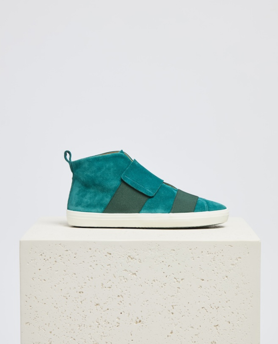 A teal suede high-top sneaker with a white rubber sole, featuring wide, overlapping velcro straps and a pull tab at the heel.