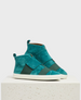 A pair of teal suede high-top sneakers with white rubber soles, featuring wide tonal elastic straps across the front and a pull tab at the heel, displayed on a textured white pedestal. 1