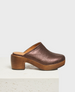 A espresso brown, metallic clog mule with a closed toe, wooden block heel, and smooth leather interior. 1