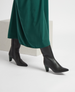 A pair of sleek, dark navy leather knee-high boots with a pointed toe and a mid-height heel, worn with a flowing green skirt. 3