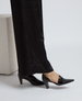 A sleek, black, pointed-toe shoe with a glossy finish and a mid-height, angular heel, worn with black pants. 5