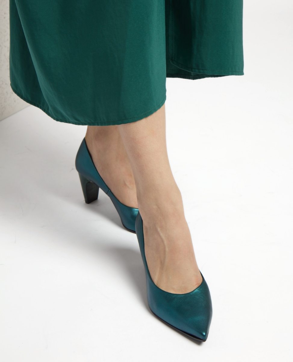A pair of elegant, teal-metallic high-heeled shoes with a pointed toe and a smooth, glossy finish, worn with a green dress.