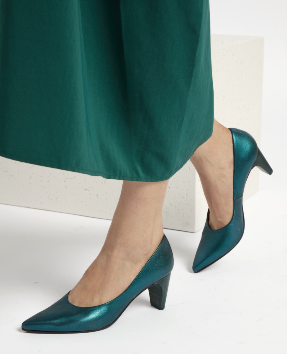 A pair of elegant, teal-colored, mid-heel pumps with a glossy finish, featuring a pointed toe and a smooth, sleek texture, complementing a long, flowing green skirt.