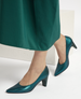 A pair of elegant, teal-colored, mid-heel pumps with a glossy finish, featuring a pointed toe and a smooth, sleek texture, complementing a long, flowing green skirt. 3