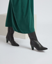 A pair of sleek, black leather knee-high boots with a pointed toe and a mid-height block heel, worn with a flowing green skirt. 6