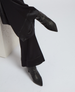 A pair of sleek, black, pointed-toe high-heeled boots with a smooth, glossy finish, worn with flowing black pants. 5