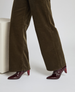 A pair of dark red, glossy, pointed-toe high-heeled shoes with a sleek, patent leather finish and a unique triangular heel design, worn with brown corduroy pants. 5