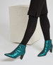 Teal, metallic ankle boots with a pointed toe, mid-height block heel, and a smooth, shiny texture, worn with black tights. 2