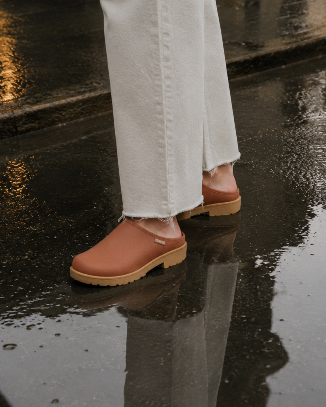 Rust color  rain clog slide with light brown rubber sole worn with white jeans on a rainly day