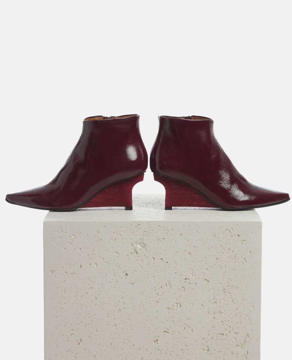 Pair of burgundy ankle boots on a light gray pedestal against a white background