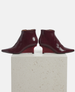 Pair of burgundy ankle boots on a light gray pedestal against a white background 4
