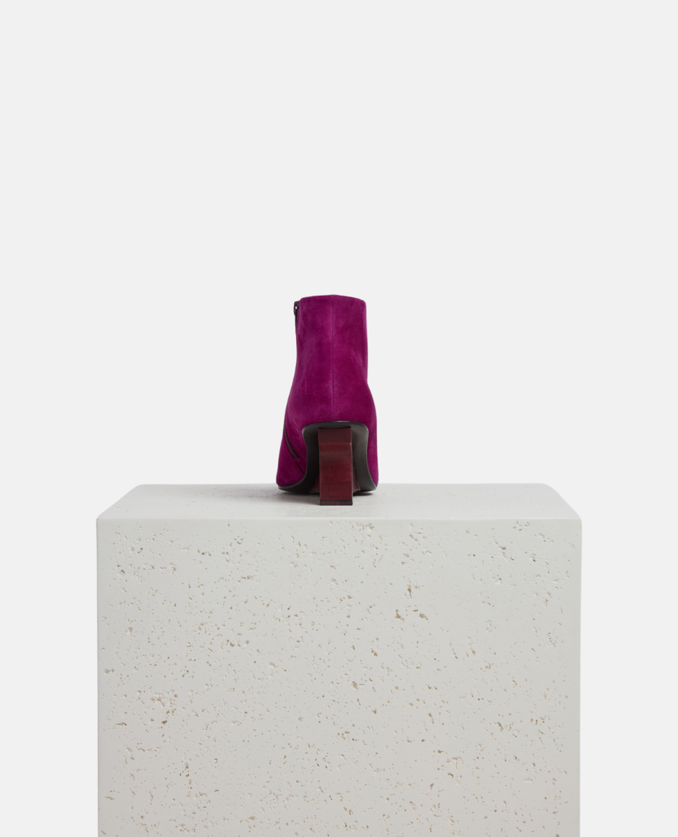 Purple suede boot on a white pedestal with a white background