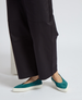 Teal suede slip-on shoes with a rounded toe and thick white rubber soles, worn with black wide-leg pants. 3