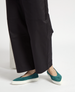 Teal suede slip-on shoes with a pointed toe and thick white rubber soles, worn with black wide-leg pants. 3