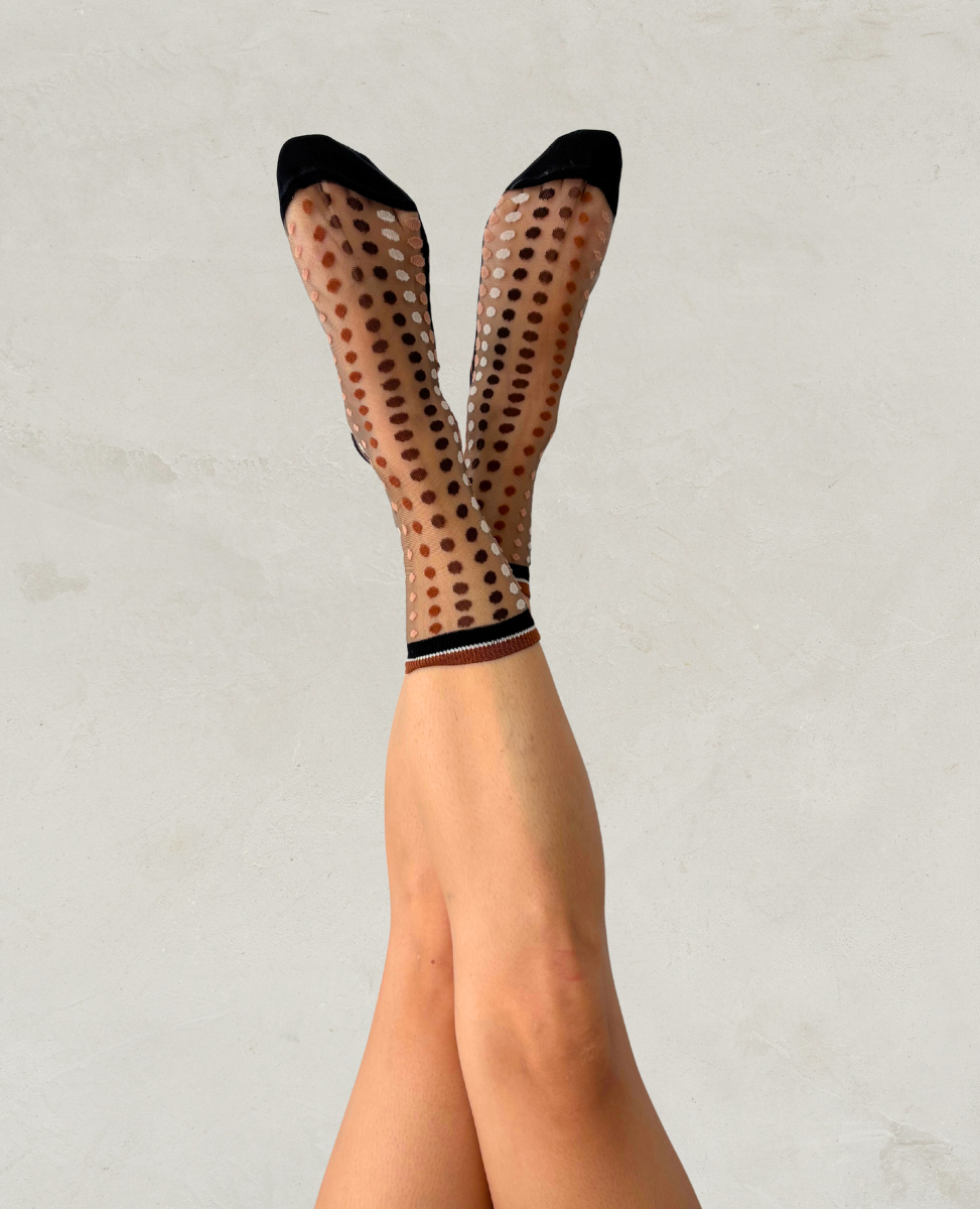 Transparent socks with black polka dots worn by a person on a light gray background