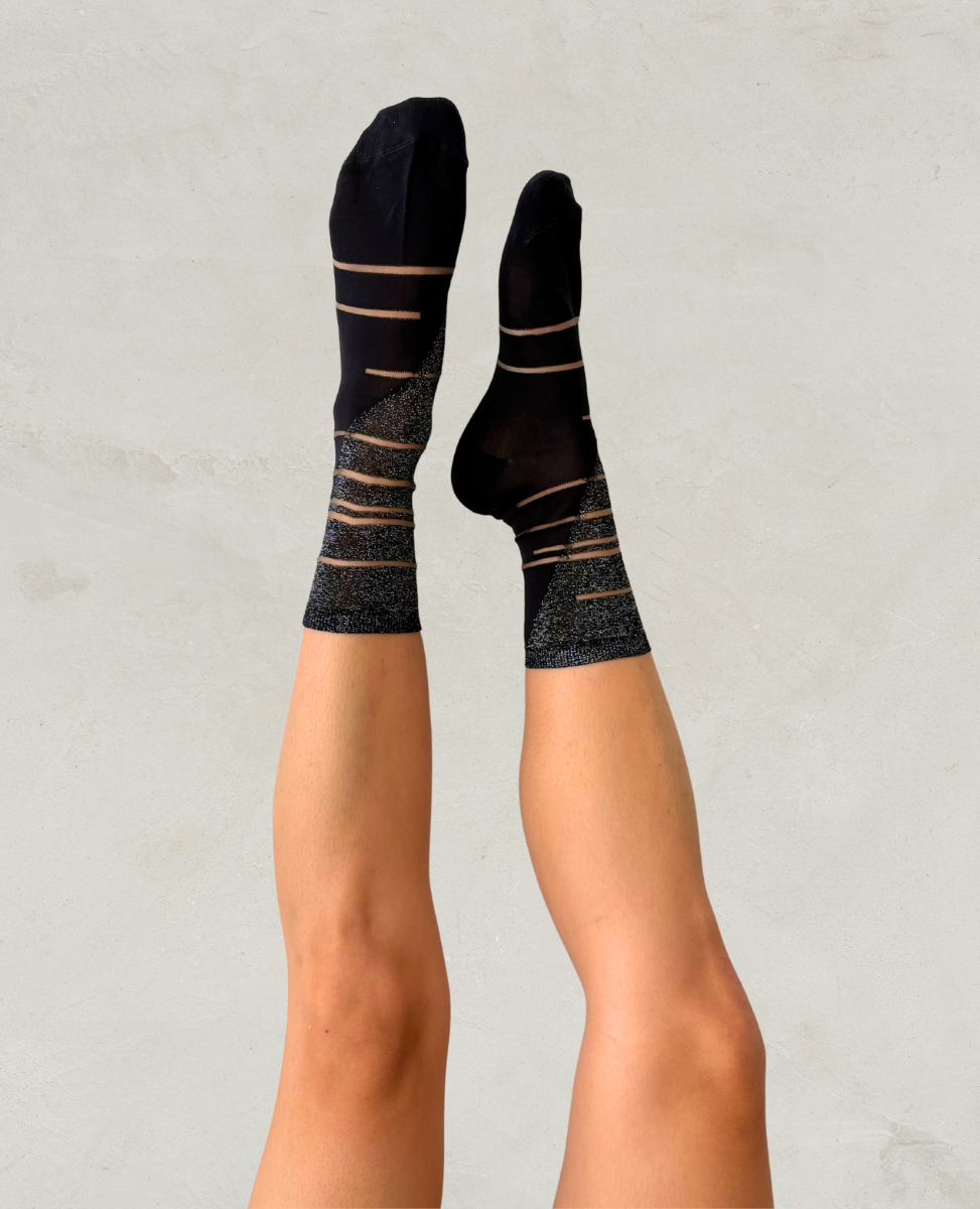 Black socks with gold stripes worn by a person on a light gray background
