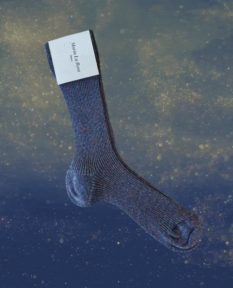 A single, long, ribbed sock in a deep blue color with subtle multicolored speckles, featuring a soft, textured fabric and a white label attached near the top.