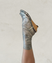 A metallic silver sock with a ribbed texture is worn with a wooden wedge sandal featuring crisscrossing silver straps. 2