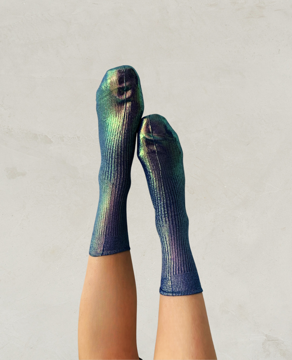 A pair of iridescent socks with a ribbed texture, displaying a gradient of blue, green, and purple hues, worn on feet against a neutral background.