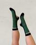 A pair of mid-calf socks featuring a green body with a subtle checkered pattern, black toe and heel caps, and beige accents at the ankle and sole, made from a soft, stretchy fabric. 1