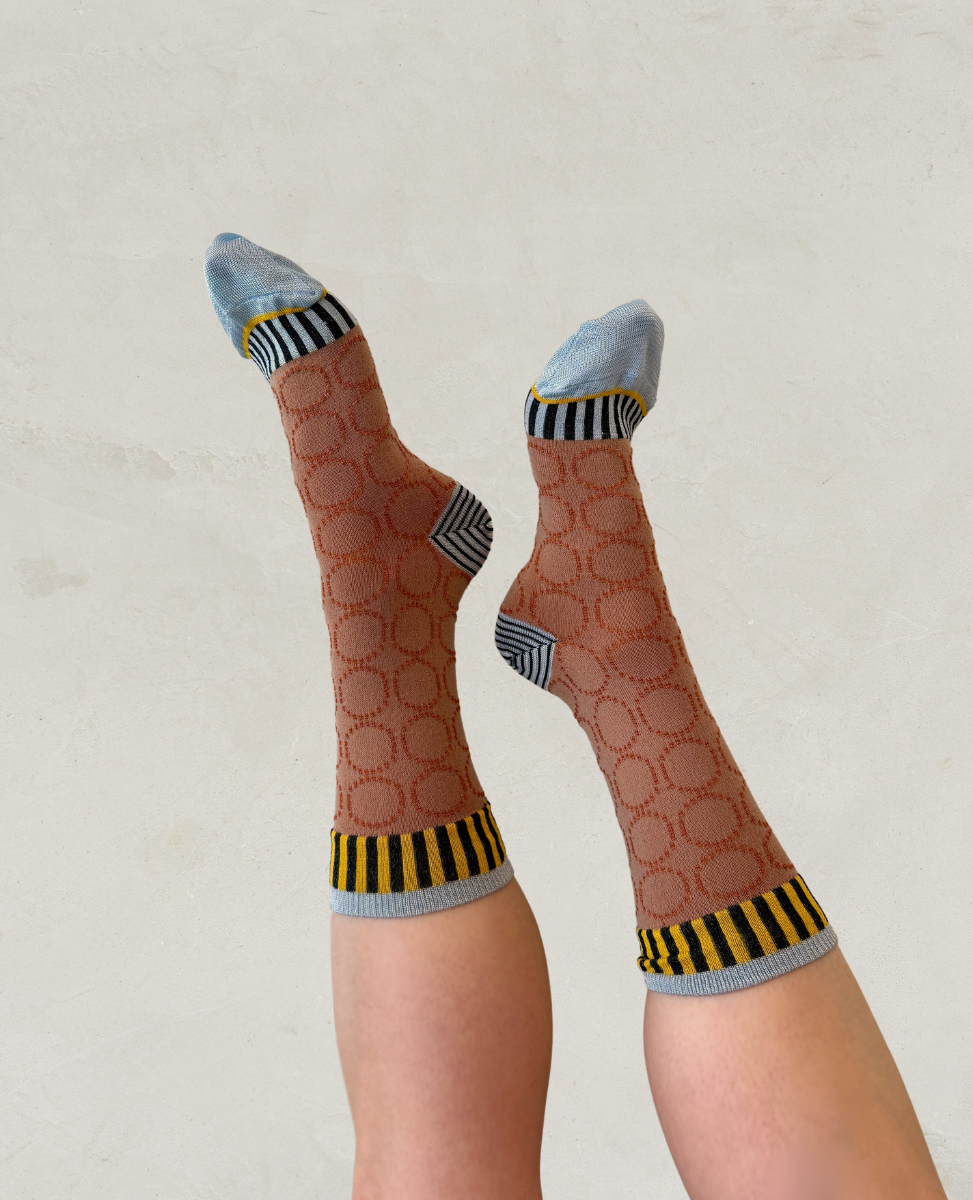 Sheer brown socks with a circular pattern, featuring light blue toes and heels, and black and yellow striped cuffs.