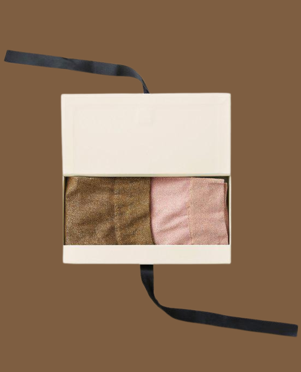 A cream-colored rectangular box with a black ribbon contains three folded, textured fabric items in shades of brown and pink.