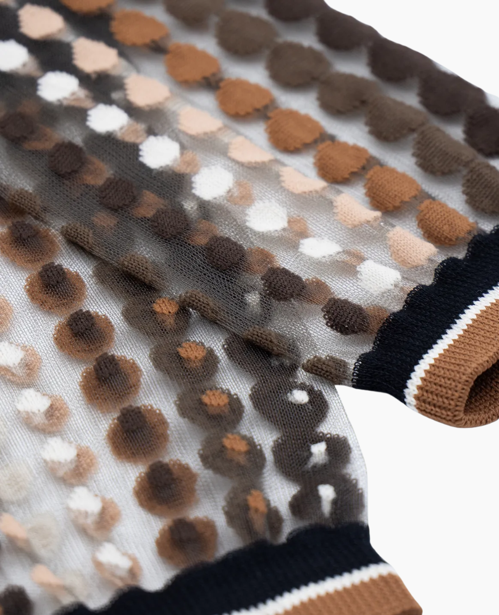 Close-up of a patterned fabric with brown, beige, and white dots on a black background.