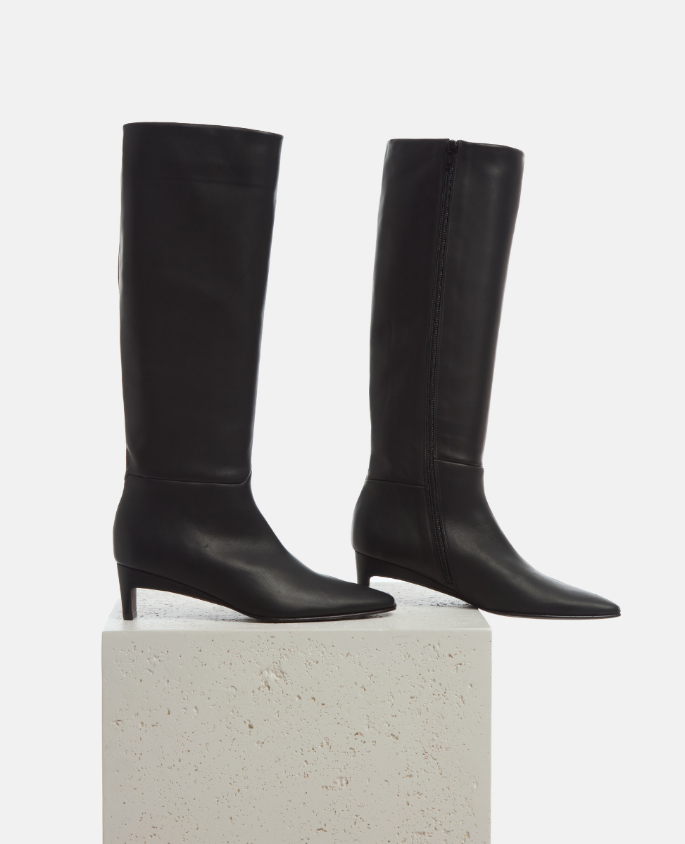 Pair of black knee-high boots on a light gray pedestal against a white background