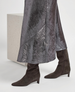 Person wearing a metallic silver skirt and brown knee-high boots on a white background 5