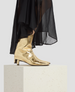Gold metallic boots worn with a black sheer skirt on a light gray background 5