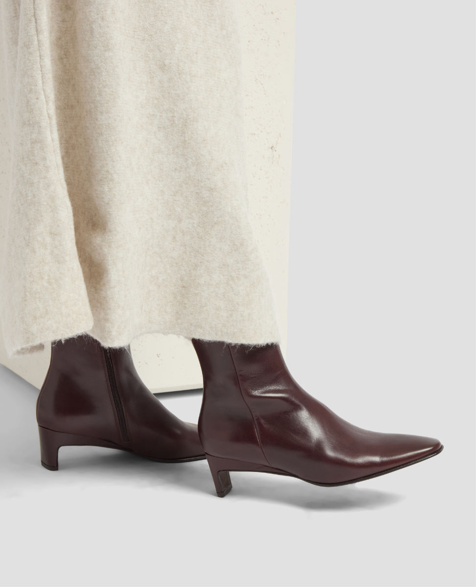 Brown leather ankle boots worn with a cream sweater on a light gray background