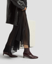 Person wearing a black coat, sheer black skirt, and brown ankle boots on a light gray background 5