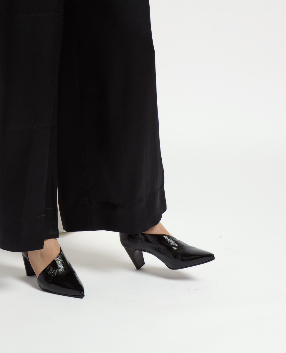 A pair of sleek, black patent leather pointed-toe heels with a low, block heel and a glossy finish.