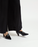 A pair of sleek, black patent leather pointed-toe heels with a low, block heel and a glossy finish. 1