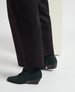 Dark green, ankle-high suede boots with a pointed toe and a low, angled block heel, paired with black pants. 1