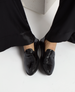 Shiny black leather loafers with a sleek, smooth texture and a low heel, featuring a minimalist design and rounded toe. 1