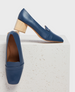 A pair of elegant blue leather loafers with a sleek, pointed toe and a distinctive light wooden block heel, featuring a smooth texture and a subtle seam detail across the upper. 1