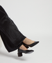 A pair of sleek, black patent leather heels with a pointed toe and a low, chunky heel, worn with black pants. 1