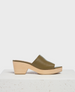 A stylish sandal featuring an olive green leather upper with a smooth texture, an open toe design, and a light wooden wedge heel, resting on a textured white surface. 3