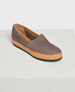 A sleek, slip-on shoe with a smooth gray upper, contrasting orange sole, and a minimalist design featuring a slightly pointed toe and low profile. 1