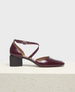 A burgundy patent leather shoe with a low block heel, pointed toe, and a crisscross ankle strap featuring a small silver buckle. 1